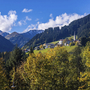Berge und ein Dorf mit Kirche im grünen Tal unter blauem Himmel.