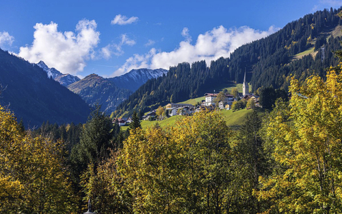 Berge und ein Dorf mit Kirche im grünen Tal unter blauem Himmel.
