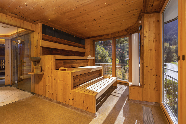 Holzsauna mit Fenstern und Blick auf bewaldete Berge.