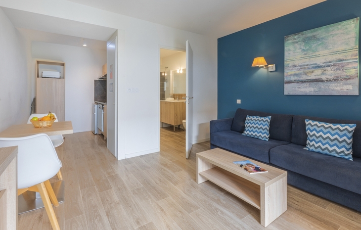 Wohnzimmer mit blauer Couch, Holztisch, Stühlen und Wandkunst.