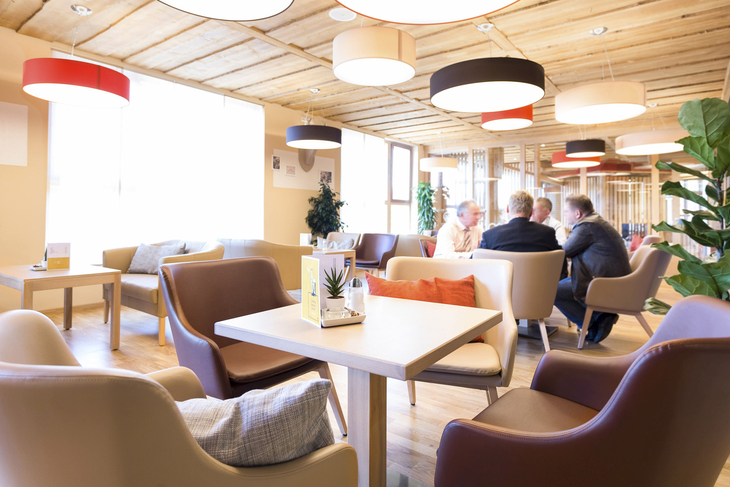 Hotel-Lounge mit hellen, modernen Möbeln und mehreren Gästen.