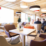 Hotel-Lounge mit hellen, modernen Möbeln und mehreren Gästen.